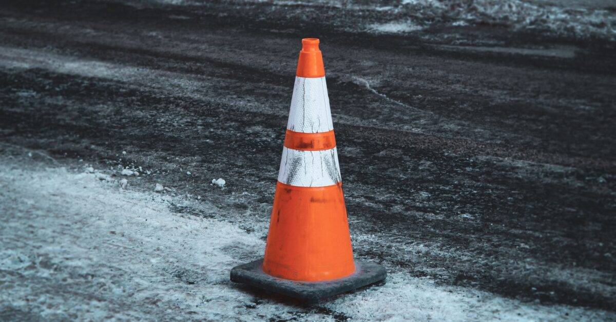 orange and white traffic cone on black sand